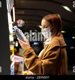 Kaukasische Frau Kunden, die Gesichtsschutzmaske am Flughafen tragen, Wasserflaschen kaufen und wählen, lesen Informationen auf einem Etikett. Einkauf von Lebensmitteln d Stockfoto