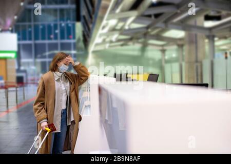 Frau mit Gepäck wegen Stornierung des Flugs verärgert, steht an leeren Check-in-Schaltern am Flughafenterminal wegen Coronavirus-Pandemie/Covid-19-Outb Stockfoto