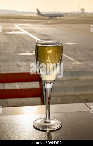 Ein Glas Champagner auf einem Tisch in einer Flughafenlounge mit einem Flugzeug, das im Hintergrund platzt Stockfoto