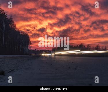Spektakulärer, heller Himmel bei Sonnenuntergang. Bei längerer Belichtung fotografierte Autoleuchten. Russland. Stockfoto