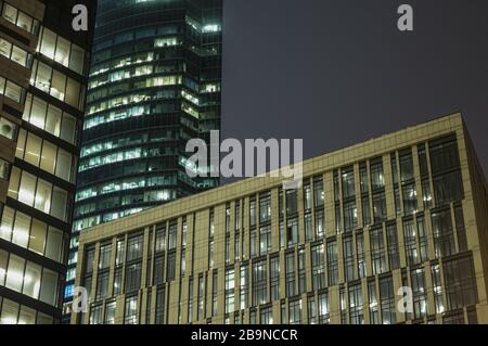 Abstraktes High-Tech-Hintergrundfragment moderner Fassadengebäude aus Stahl und Glas mit nächtlichen Lichtern in den Fenstern. Stockfoto