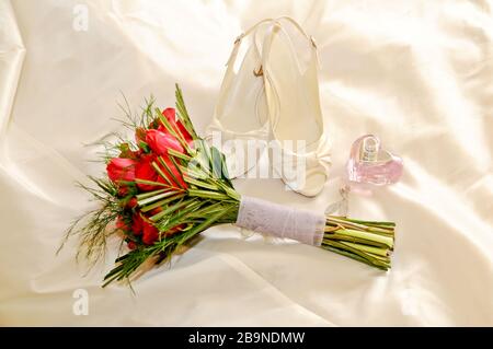 Schuhe einer Braut zusammen mit anderen Accessoires wie Ohrringe, Parfüm und ein Blumenstrauß. Stockfoto