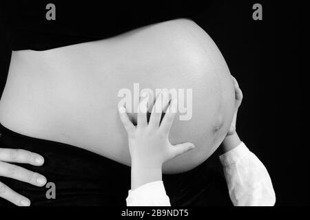 Schwarz-weißes Bild des Bauch einer schwangeren Frau mit kleinen Händen unterstützt. Stockfoto