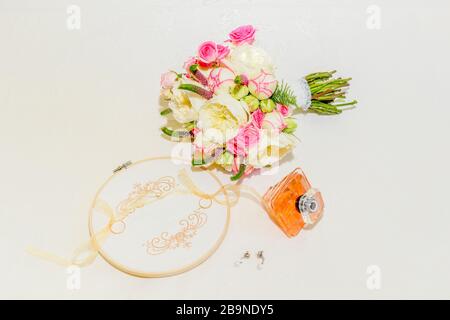 Strauß Rosen und weiße und rosa Pfingstrosen neben Rahmen mit Ringen, Ohrringen und Duft einer Braut Stockfoto