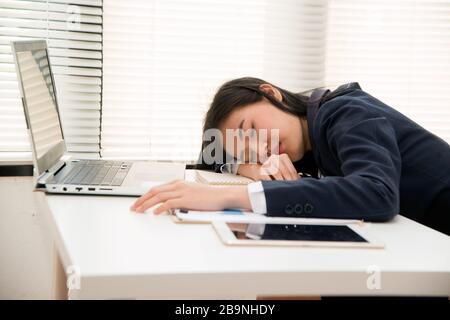 Junge asiatische Geschäftsfrau schläft im Büro auf dem Tisch, weil sie überarbeitet, von Arbeitsüberlastung gestresst und eine müde und schläfrige Dame ist. Stockfoto