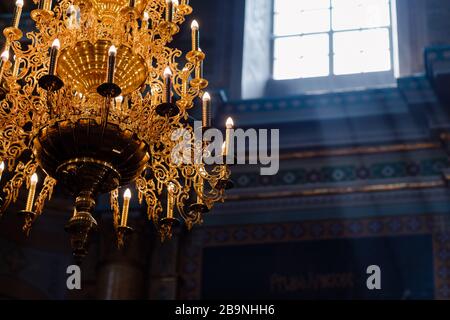Großer Kronleuchter aus Bronze mit elektrischen Kerzen in der christlichen Domkirche. Tageslicht aus dem Fenster in der Kirche. Selektiver Fokus Stockfoto