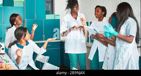 Weibliche afrikanische Medizinstudenten, junge Absolventen oder Ärzte diskutieren über das laufende Projekt. Energetische ausdrucksstarke Gruppendiskussion in Testlabors Stockfoto