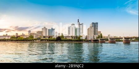 Panoramablick auf die Skyline von Frankfurt am Main mit Wolkenkratzern, Promenade und Brücke über den Main in der Innenstadt bei Sonnenuntergang. Moderne Architektur Stockfoto