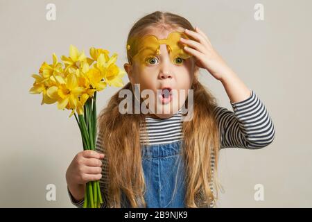 Wenig überraschtes Kindermädchen im Strohhut mit einem Blumenstrauß gelber Blumen. Mummys kleiner Helfer im Garten. Platz für Text kopieren Stockfoto