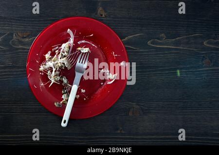 Fischknochen auf einer einzigen roten Platte. Holztisch Hintergrund. Flaches Foto oben unten mit Kopierbereich Stockfoto