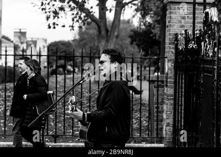 Ein Schwarzweißfoto eines Straßenmusikers, der außerhalb von Greenwich Park, England, auftrat. Stockfoto