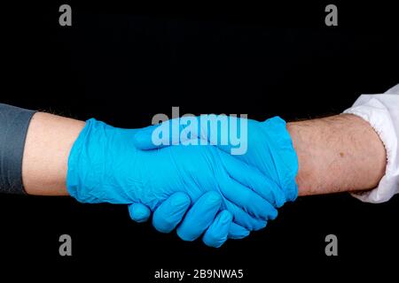 Schüttelnde Hände, zwei Personen, die blaue Latexhandschuhe tragen, schütteln die Hände. Nur Hände sichtbar. Nahansicht, schwarzer Hintergrund. Stockfoto
