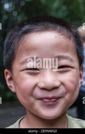 Chongqing, China - 9. Mai 2010: Im Zoo oder im Tierpark. Nahaufnahme des lächelnden Jungen vor dem Teenager-Kind vor dunkelgrüner Laubenkulisse. Stockfoto