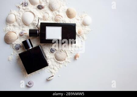 Zwei schwarze Parfümflaschen aus Glas auf Sand mit Meeresschalen und Jakobsmuscheln Stockfoto