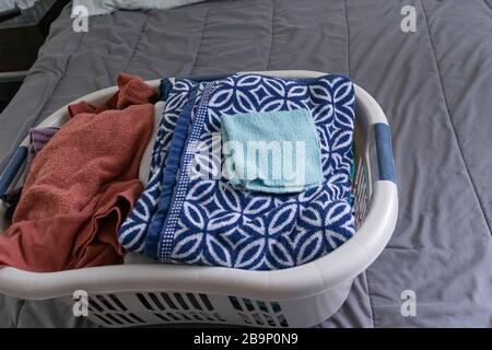 Frisch gewaschene Kleidung in einem Wäschekorb, der auf einem Bett gefaltet werden muss. Stockfoto