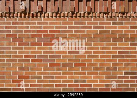 Hervorstehende Ziegelsteine in geometrischer Form schmücken die Oberseite dieses traditionellen rotbraunen Wandtexturhintergrunds aus Backstein mit Sonnenlicht gegossener Schatten Stockfoto