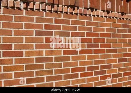 Hervorstehende Ziegelsteine in geometrischer Form schmücken die Oberseite dieses traditionellen rotbraunen Wandtexturhintergrunds aus Backstein mit Sonnenlicht gegossener Schatten Stockfoto