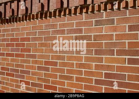 Hervorstehende Ziegelsteine in geometrischer Form schmücken die Oberseite dieses traditionellen rotbraunen Wandtexturhintergrunds aus Backstein mit Sonnenlicht gegossener Schatten Stockfoto