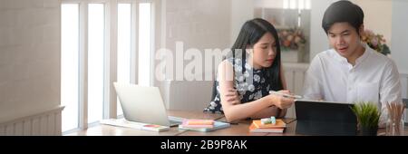 Ein Foto von zwei Studenten, die sich bei ihrem Projekt beraten, während sie an einem komfortablen Arbeitsplatz sitzen Stockfoto