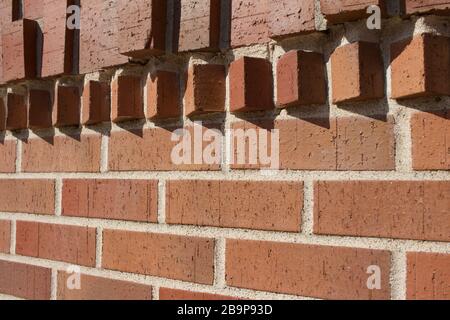 Hervorstehende Ziegelsteine in geometrischer Form schmücken die Oberseite dieses traditionellen rotbraunen Wandtexturhintergrunds aus Backstein mit Sonnenlicht gegossener Schatten Stockfoto