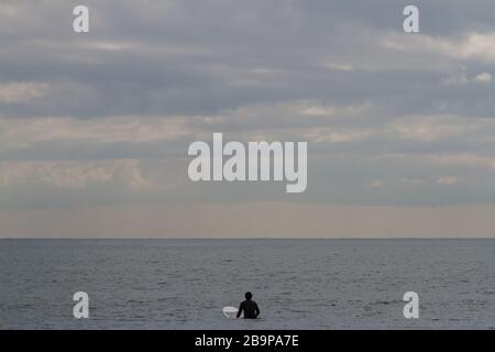 Ein Surfer sitzt auf seinem Surfbrett und wartet auf Wellen am Enoshima Beach, Kanagawa, Japan. Stockfoto