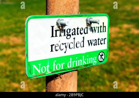 Selektiver Fokus. Bewässert mit recyceltem Wasser, kein Warnschild trinken, das im Freien mit verschwommenen Feldhintergründen angebracht ist. Das verwitterte Schild ist leicht Stockfoto