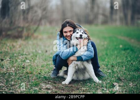 Junge Frau spielt mit dem Husky-Hund für einen Spaziergang im Frühlings-Wald, lacht lustig, glücklich mit Haustier Stockfoto