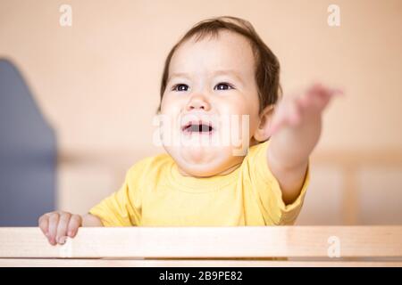 Baby dunkel belästigt im Kinderbett stehen und schreien sie nach Kamera in gelbem T-Shirt Stockfoto