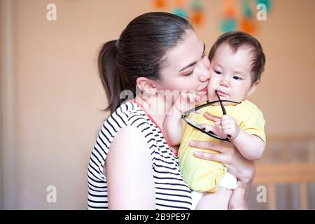 Schöne junge Mutter küsst und verwöhnt ihr Baby. Gemischte Rasse kasachisch Stockfoto
