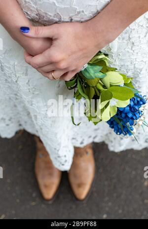 Eine andere Frau, die Cowboystiefel trägt und hausgemachtes Blumenstrauß aus Papier hält Stockfoto