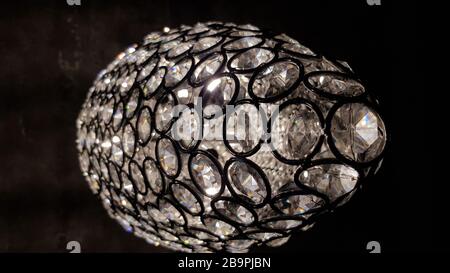 Leuchtende Schuppen mit kristallklaren runden Elementen im Inneren. Glänzende Oberfläche des Glaskronleuchters. Die moderne Lampentextur aus glitzerndem Glas sieht wie ein Disco-Ball aus. Stockfoto