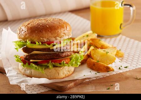 Ein Burger mit doppeltem Fleisch und Käse serviert mit Kartoffelkeilen und Orangensaft Stockfoto