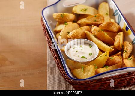 Eine Portion Kartoffelkeile wird in einem Rattankorbtablett mit Mayonnaisesauce mit einem Besprühen von Petersilienblättern serviert Stockfoto