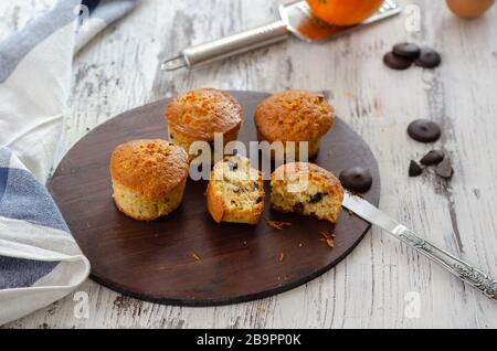 Muffin mit Orange auf einem Holztisch. Süße Gebäckstücke auf dem Brett, Draufsicht. Stockfoto