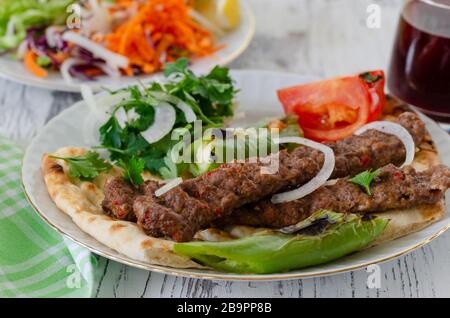 Traditionelles Adana Kebap mit Tomaten und Salat auf einem Fladenbrot als Draufsicht. Stockfoto