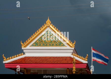 Atemberaubendes Detail eines buddhistischen Tempels mit der thailändischen Flagge, die im Wind weht, gegen einen schwarzen Himmel voller Regen, Bangkok, Thailand Stockfoto