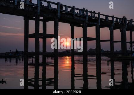 Die U-Bein-Brücke bei Sonnenuntergang, Mandalay, Myanmar. Menschen Silhouetten auf langer Holzbrücke vor farbenfrohem Himmel und Wasserhintergrund Stockfoto