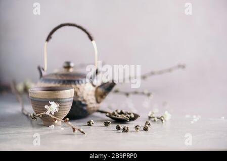 Traditionelle asiatische Teezeremonie. Flache Lage aus eiserner Teekanne, Tassen und blühenden Kirschbaumblüten auf grauem Betongrund. Federkonzept Stockfoto