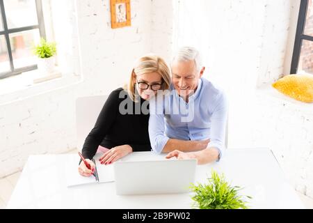 Reifes Paar, das Familienfinanzen zu Hause macht. Ein älteres Paar spricht über Hauswirtschaft, während es am Schreibtisch sitzt und einen Laptop verwendet. Stockfoto