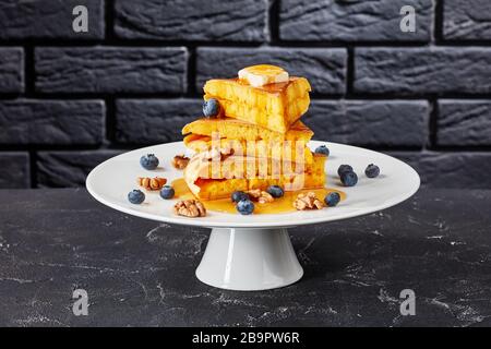 Honig wurde über einen Stapel von Scheiben aus Hok lo Pfanne gegossen, Schwammpfannkuchen mit Butter, Blaubeeren und Walnüssen auf einem Kuchenständer mit schwarzem Backstein mit Stockfoto