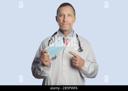 Ein Arzt in einem medizinischen Mantel und ein Stethoskop auf seinen Schultern zeigt eine medizinische Maske Stockfoto