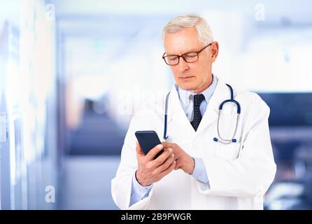 Portrait des männlichen Oberarztes mit Handy und SMS im Krankenhaus. Stockfoto