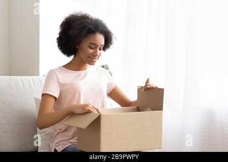 Zufriedene junge Frau Kunde sitzt auf dem Sofa und packt Paketpaket aus Stockfoto