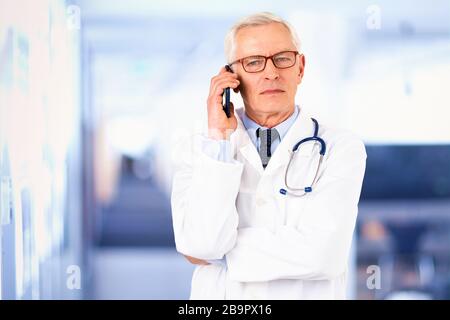 Portraitaufnahme eines älteren männlichen Arztes, der einen Anruf macht, während er in der Arztpraxis steht. Stockfoto
