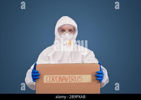 Arzt in Schutzanzug und Maske stehend mit Box in den Händen Stockfoto