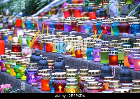 Kirchenlaternen und Kerzen in Erinnerung an Verstorbene. Verschiedene Farben Kerzen auf Stufen. Glaslaternen. Stockfoto