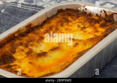 Beef Lasagne oder Lasagne zubereitete, tiefgefrorene Mahlzeit, die in einem Metallbackblech auf einem blauen Teehandel zubereitet wird. Fast-Food-Konzept Stockfoto