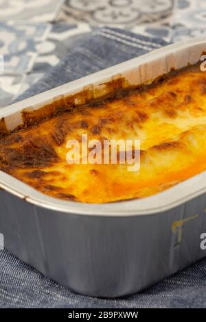 Beef Lasagne oder Lasagne zubereitete, tiefgefrorene Mahlzeit, die in einem Metallbackblech auf einem blauen Teehandel zubereitet wird. Fast-Food-Konzept Stockfoto