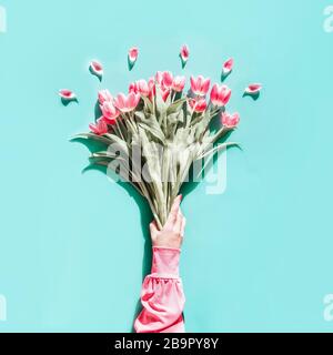 Weibliche Hand in rosafarbener Bluse mit hübschen Tulpen auf helltürkisfarbenem Hintergrund. Draufsicht. Flaches Lay. Muttertag Gruß Stockfoto