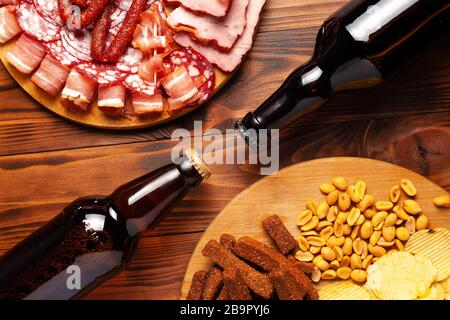 Zwei Flaschen Bier und verschiedene Snacks für jeden Geschmack auf Holzgrund. Fleischprodukte, Wurstscheiben, Pommes, Nüsse, Croutons. Stockfoto